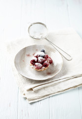 Little mascarpone tart with fresh raspberries on wooden background.