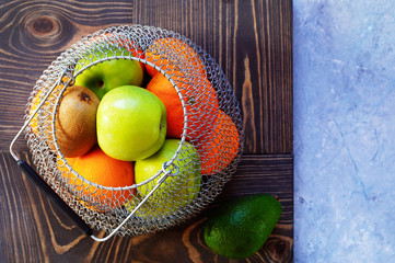 Apples, oranges, kiwis, avocados in a basket of woven metal cells. Reusable bag, zero waste. Concept of nature conservation. Top view, copy space..