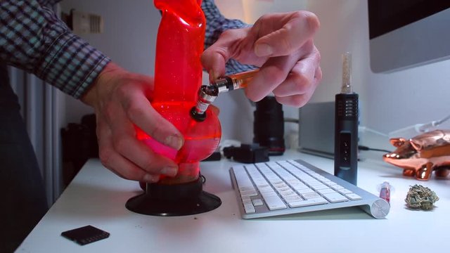 The designer smokes a cannabis bong at the table. A light flashes in the red bong. The concept of psychological relaxation of a person.