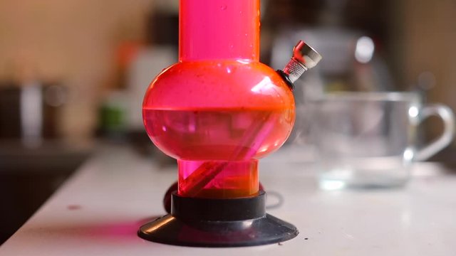 Close-up of smoking red bong. A man smokes cannabis and exhales smoke. Drug use concept.