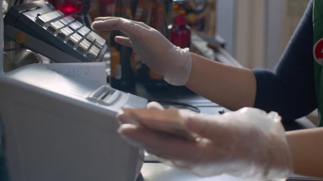 Close up checkout counter in the supermarket during coronavirus epidemic. Hands of the cashier in protective gloves take cash and put it in a cash box. COVID-19 pandemic
