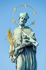 Statue of saint with cross at the Charles Bridge in Prague at blue gradient sky, Czech Republic, summer time