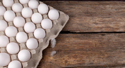 White chicken eggs in tray and two small feathers near on an old wooden table.