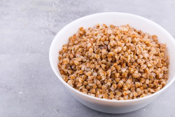 Cooked buckwheat in white ceramic bowl on grey background. Top view, horizontal format.