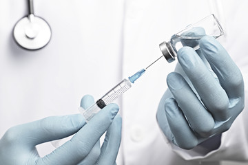 Close up doctor arm using syringe and ampoule, white robe dressed doctor on blurred background....