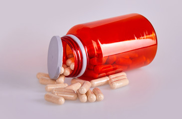 Red transparent plastic bottle with scattered capsules  in  on white background. Health supplement. 