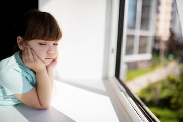 Adorable sad child girl by the window at home. Quarantine. Coronavirus. Epidemic.