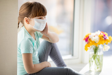 Adorable sad child girl by the window at home. Quarantine. Coronavirus. Epidemic.