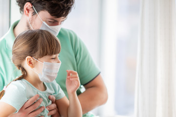 Fototapeta premium Adorable little girl and her father or doctor by the window at home or hospital. Quarantine. Coronavirus. Epidemic.