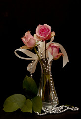 A arrangement of pink roses with ribbon and silver pearls on black background