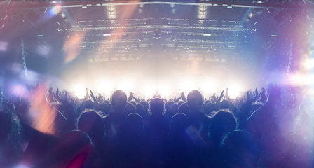 Concert crowd point of view inside a large concert hall during a music festival, the lit stage is...
