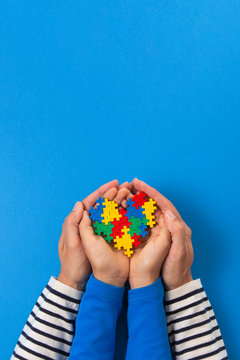World autism awareness day concept. Adult and child hands holding puzzle heart on light blue background