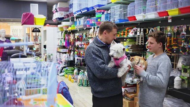 Father with teenager son and little dog choose products for animals in petshop