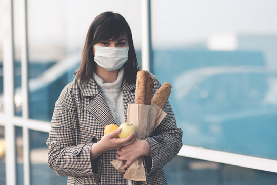 Asian woman wearing medical mask for protection from coronavirus holding food walking in city street outdoors. Looking at camera. Healthcare. Social distancing.