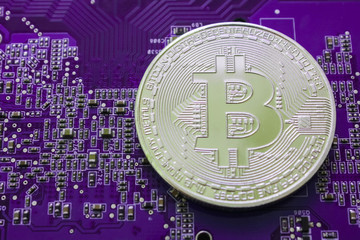 A silver bitcoin coin lies on a purple circuit board.