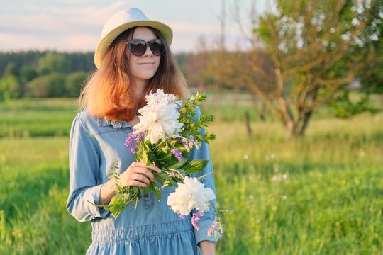 Beautiful girl in sunglasses hat with bouquet of wildflowers
