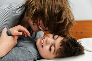 niño caucasico con pluridiscapacidad en pijama y su madre jugando, riendo, haciendo mimos,...