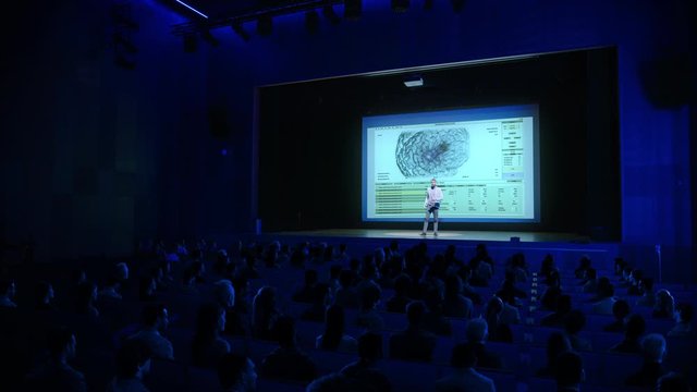On Stage: Scientific Startup CEO Shows  Healing 3D Brain Concept on Big Screen, Talks about Technology, Science, Health,  Mindfulness. Medical Industry Conference Auditorium Hall full of Participants