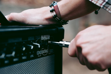 Hand inserts a cord jack into a combo amplifier for electric guitar