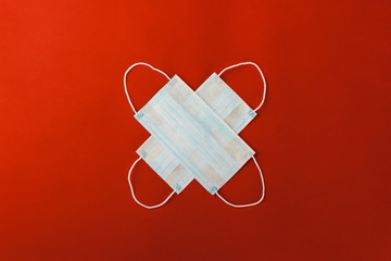 Two respiratory medical protective masks lie in the shape of a cross on a red background.