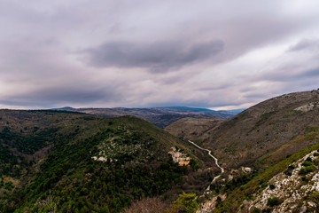 A beautiful view of the rocky French Alps mountains landscape and a road cutting through the range under the cloudy sky