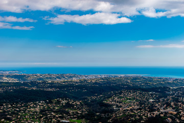 Fototapeta premium A wide / high angle panoramic view of buildings of several towns covering the low Alps mountains hills and the Mediterranean Sea coastline (French Côte d'Azur/ Provence/ Riviera)