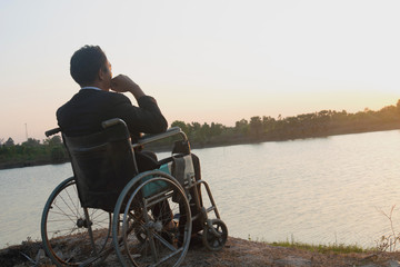 Young disabled man with river background.He is sitting on wheelchair and looking into...