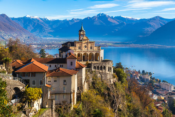 Stunning close up panorama view of Madonna del Sasso church above Locarno city with Lake Maggiore, snow covered Swiss Alps mountain peak and blue sky cloud in background in autumn, Ticino, Switzerland - obrazy, fototapety, plakaty