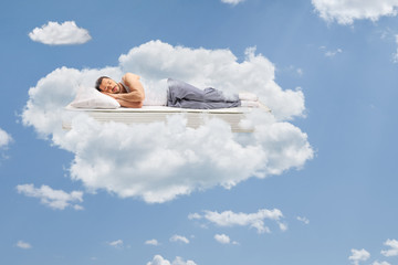 Man in pajamas sleeping on a mattress and floating in the sky