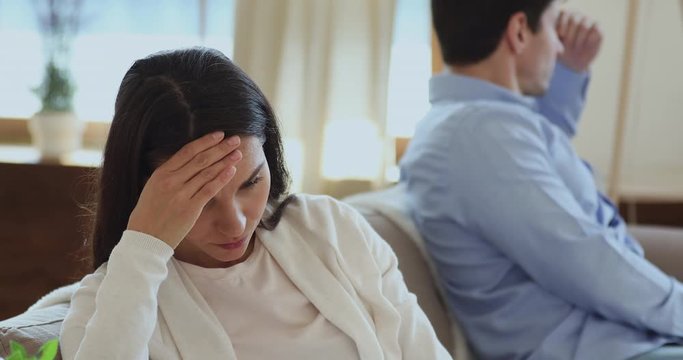 Upset wife thinking of relationship problems after fight with selfish jealous husband turned back sitting on couch. Depressed young woman feeling hurt and frustrated about unhappy marriage concept.