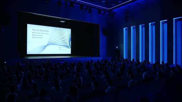 Crowd of Tech People in Cinema Theater Watching New High Tech Product Neural Network Machine Learning Software Presentation on Big Screen. Tech Industry Conference Auditorium Hall full of People