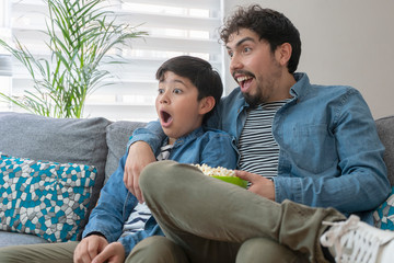 Padre e hijo asombrados viendo la tv con palomitas