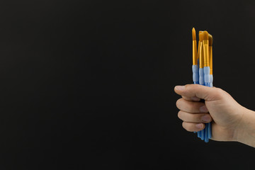 Purple paint brushes held by a hand on black background with copy space. Education, creativity, art.