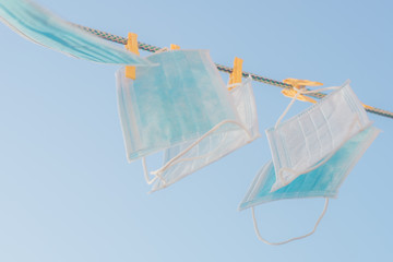 Medical face masks hang on a clothesline in blue sky background.