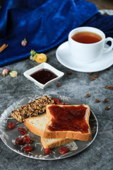 A cup of tea with chocolate toast and berry jam on a marble table, top view
