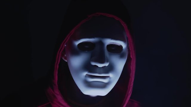 Scary hacker with mask looking to the camera. Lights flashing around him. Anonymous man coding in the dark room