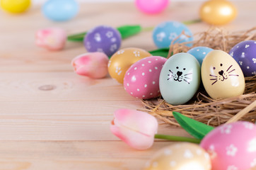 Colorful easter eggs, bunny face on egg and tulips flowers with copy space.
