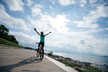 Hands free cycling woman riding Mountain Bike on sunrise seaside