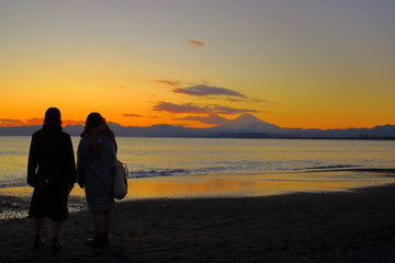夕暮れの海に佇む女性と富士山のシルエット