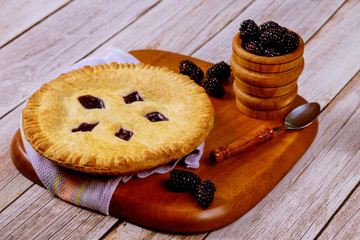 Round blackberry pie on wooden table with spoon.
