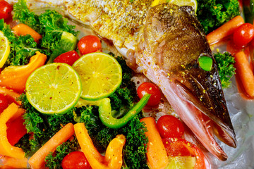 Uncooked pike with lime and vegetable in baking pan.