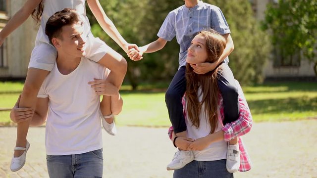 Two young kids backriding on to their parents in outdoor portrait. Young parents on vacation with kids. Family love concept. Slide from top to bottom.