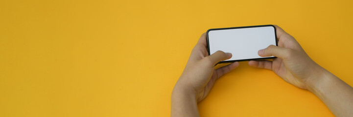 Cropped shot of a man holding horizontal blank screen smartphone on yellow background