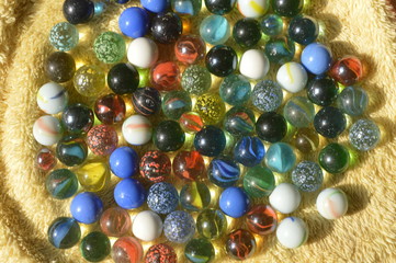 The glass balls are of many colors that are placed on a yellow cloth.