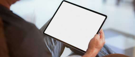 Cropped shot of a man sitting at living room and using blank screen  tablet