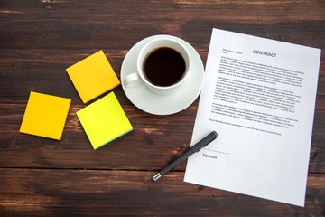 A cup of coffee and contract on wooden background