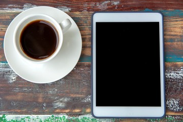 Digital tablet and coffee cup on wooden table background.