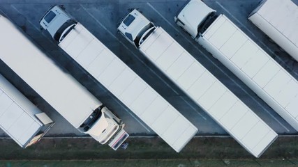 Aerial top down view of the semi trucks with cargo trailers standing for load/unload goods on the parking lot of the logistics park with warehouse, loading hub