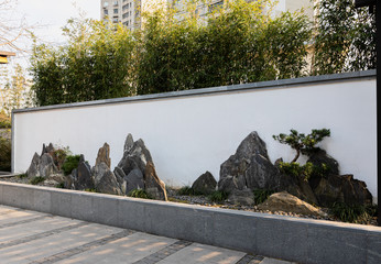 Traditional Chinese landscape painting consisting of rock slices, trees & grass in front of a white wall at public Jiangwan Park in historical, old town Jiangwanzhen, Hongkou, Shanghai, China.