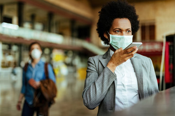 African American businesswoman wearing face mask and using voice assistant on smart phone.